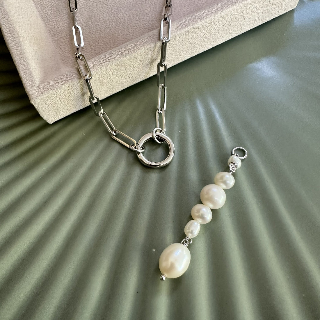 Paperlink chain necklace with a multi pearl pendant charm on a textured surface