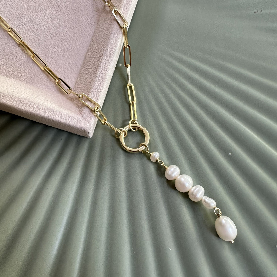 Modern statement gold necklace with natural freshwater pearl pendant on a textured surface