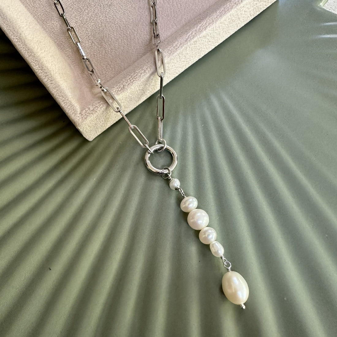 Statement Pearl Charm pendant attached to a paperclip necklace on a textured green surface