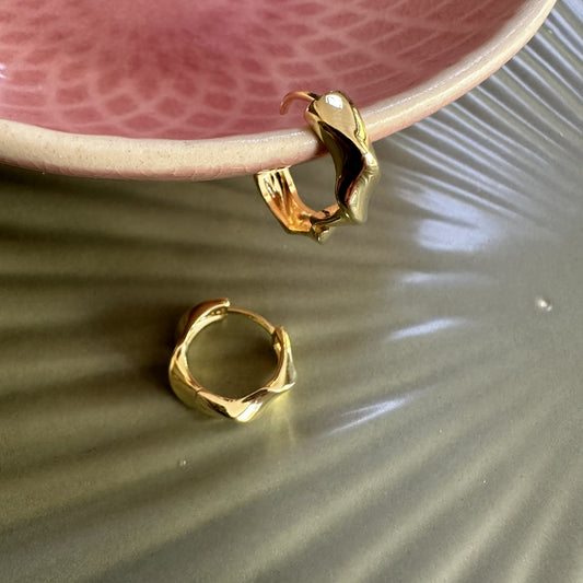 Gold chunky statment hoop earrings on a textured surface with a pink dish in the background