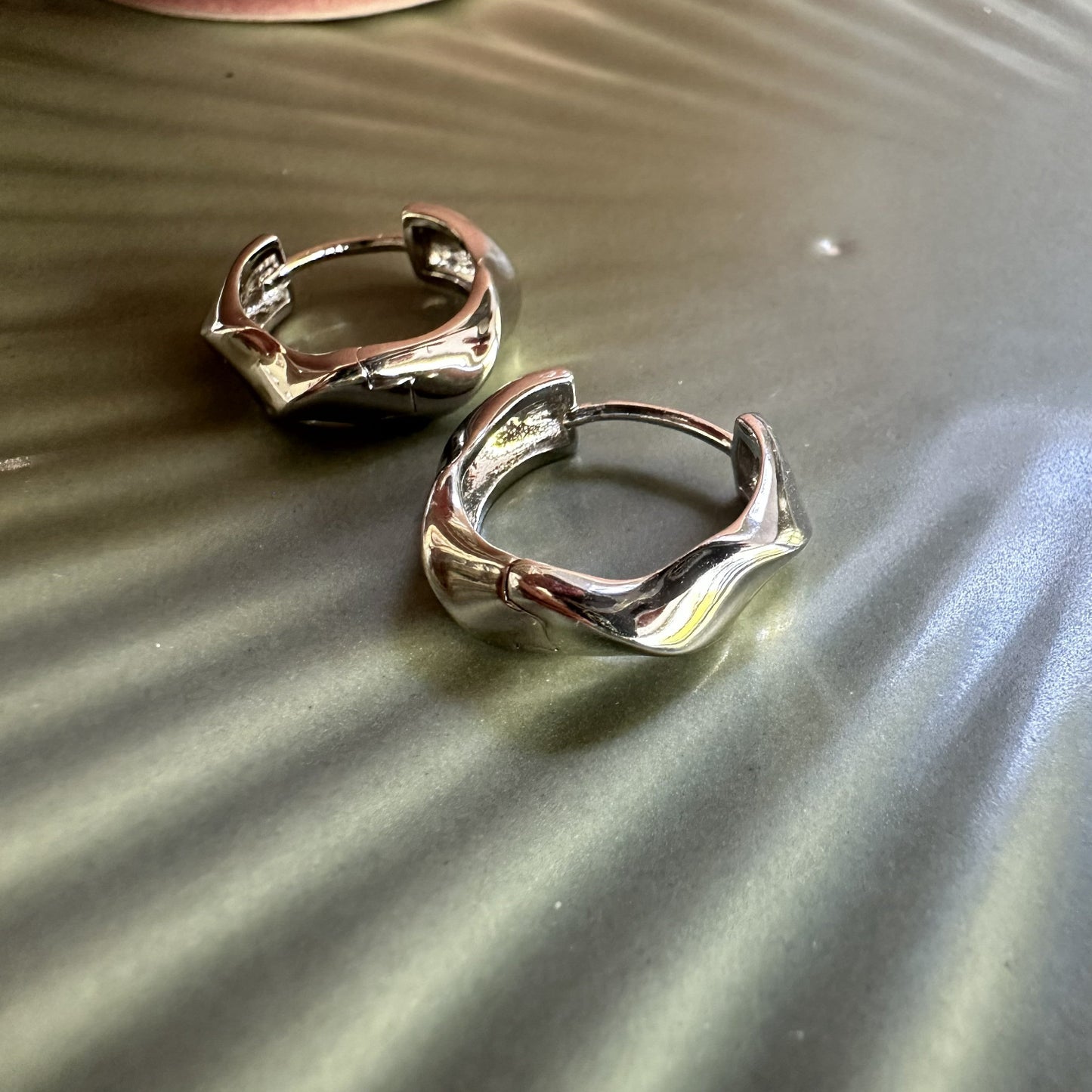 Silver chunky statement hoop earrings on a textured surface