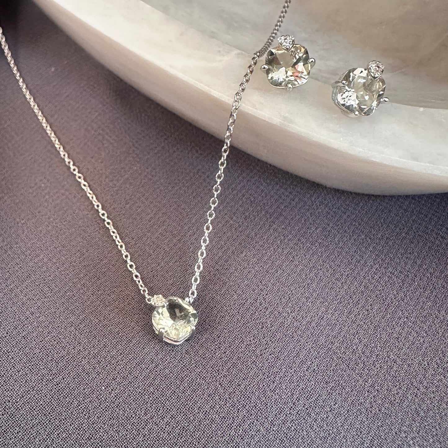Silver necklace and earrings on a gray surface with a green amethyst stone background