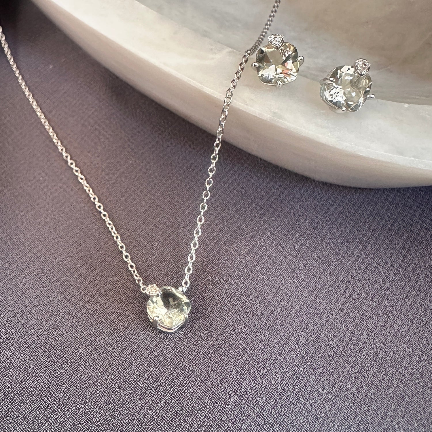 Silver necklace and earrings on a gray surface with a green amethyst stone background