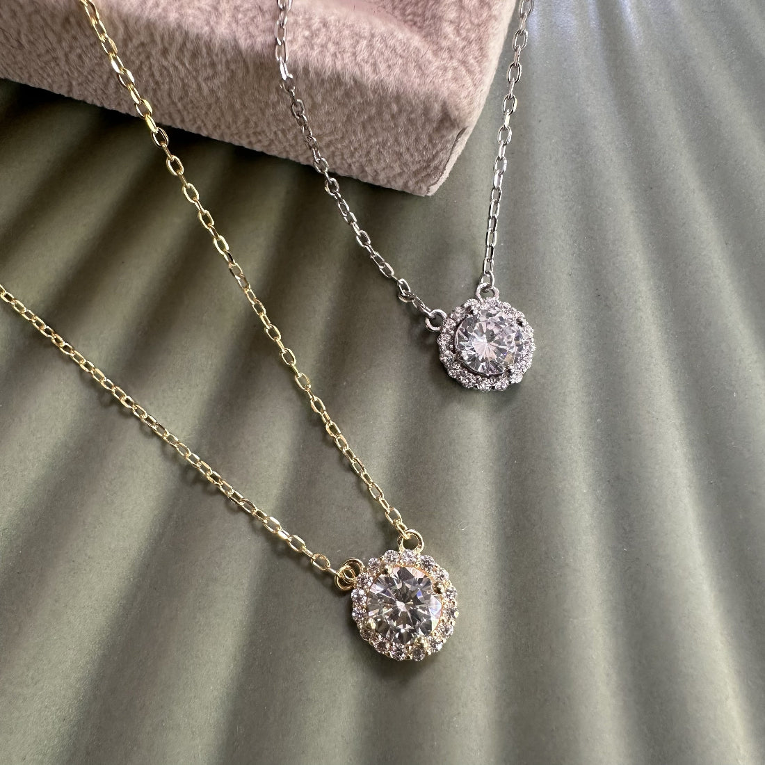 Two gemstone necklaces with halo surrounds on a textured surface