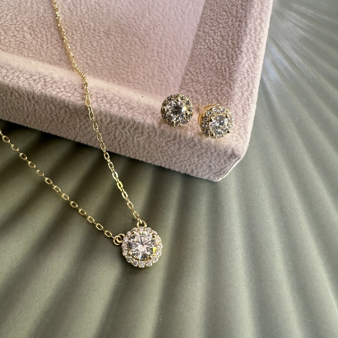 Gold necklace and earrings with cubic zirconia stones on a textured surface