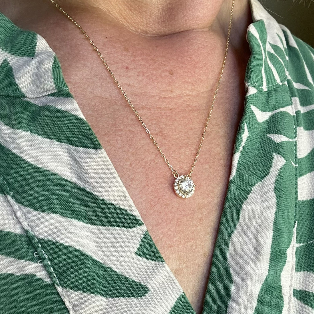Sparkly gemstone necklace with halo surround  pendant worn by a person in a green and white patterned shirt.