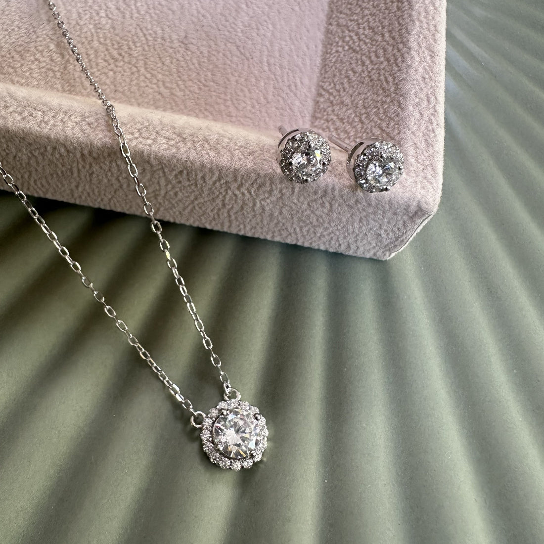 Halo gemstone silver necklace and earrings on a textured surface