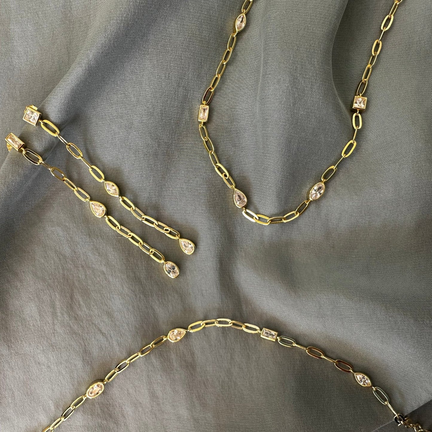 Gold jewellery set with drop earrings, bracelet and necklace with white CZ stones, on grey background