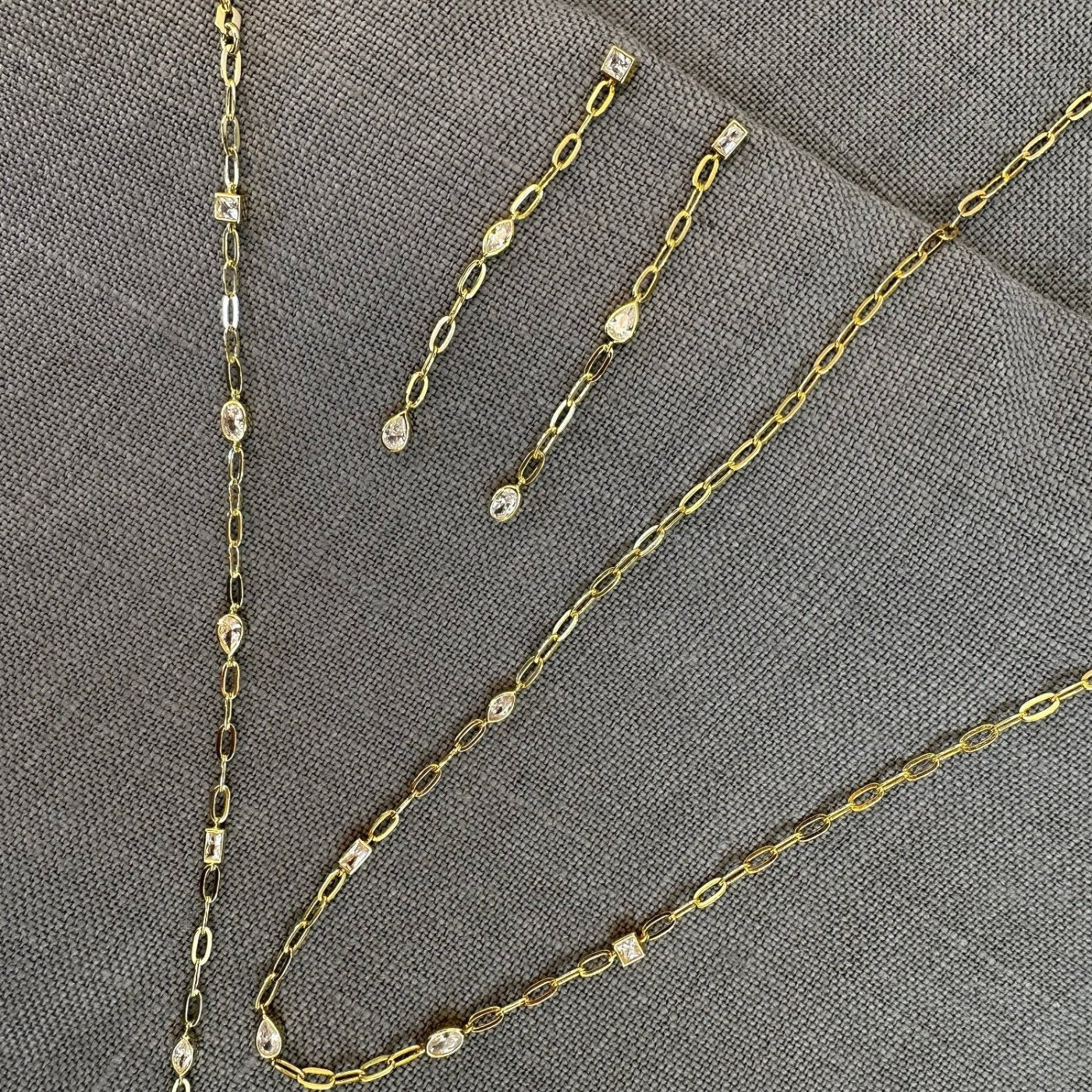 Gold set of bracelet, necklace and earrings on grey background