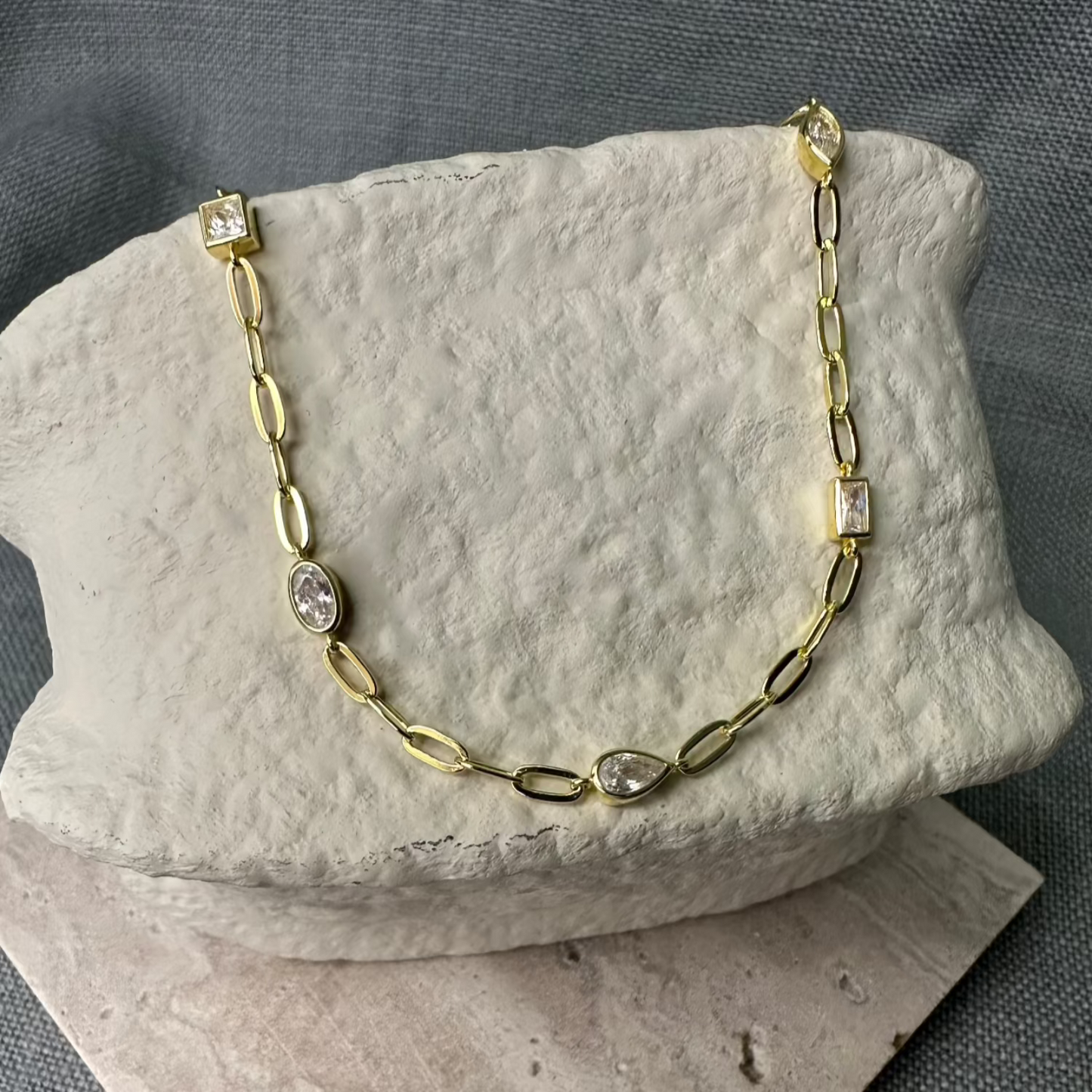 Gold Necklace with white gemstones on stone prop.