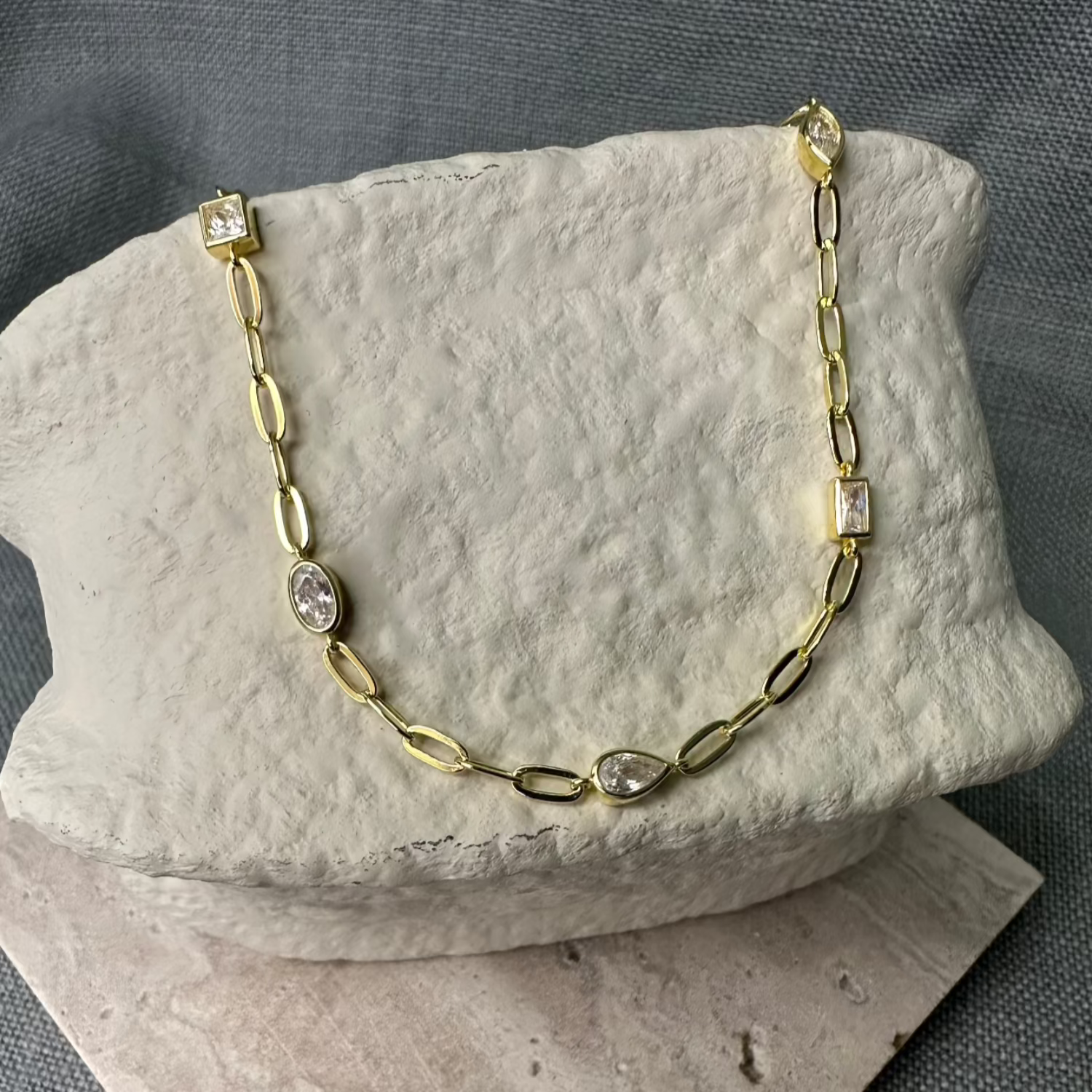 Gold Necklace with white gemstones on stone prop.