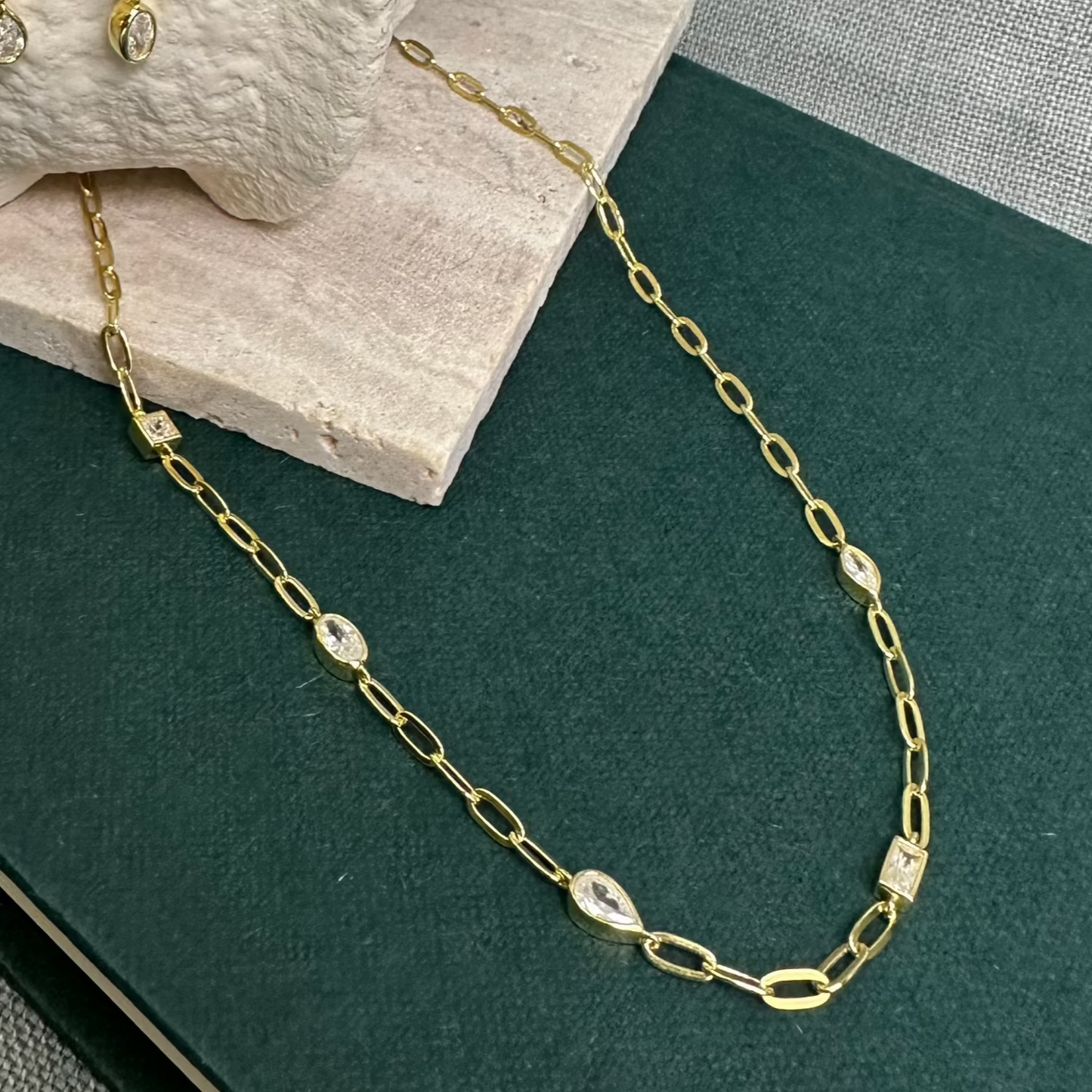 Gold Necklace with different shape CZ stones on green background