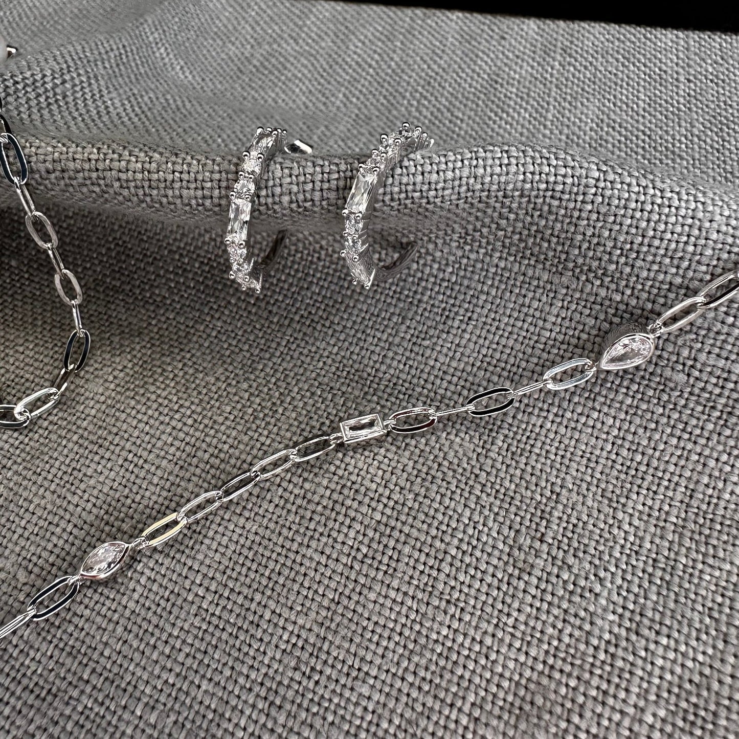 Silver hoop CZ earrings with gemstone necklace on grey background