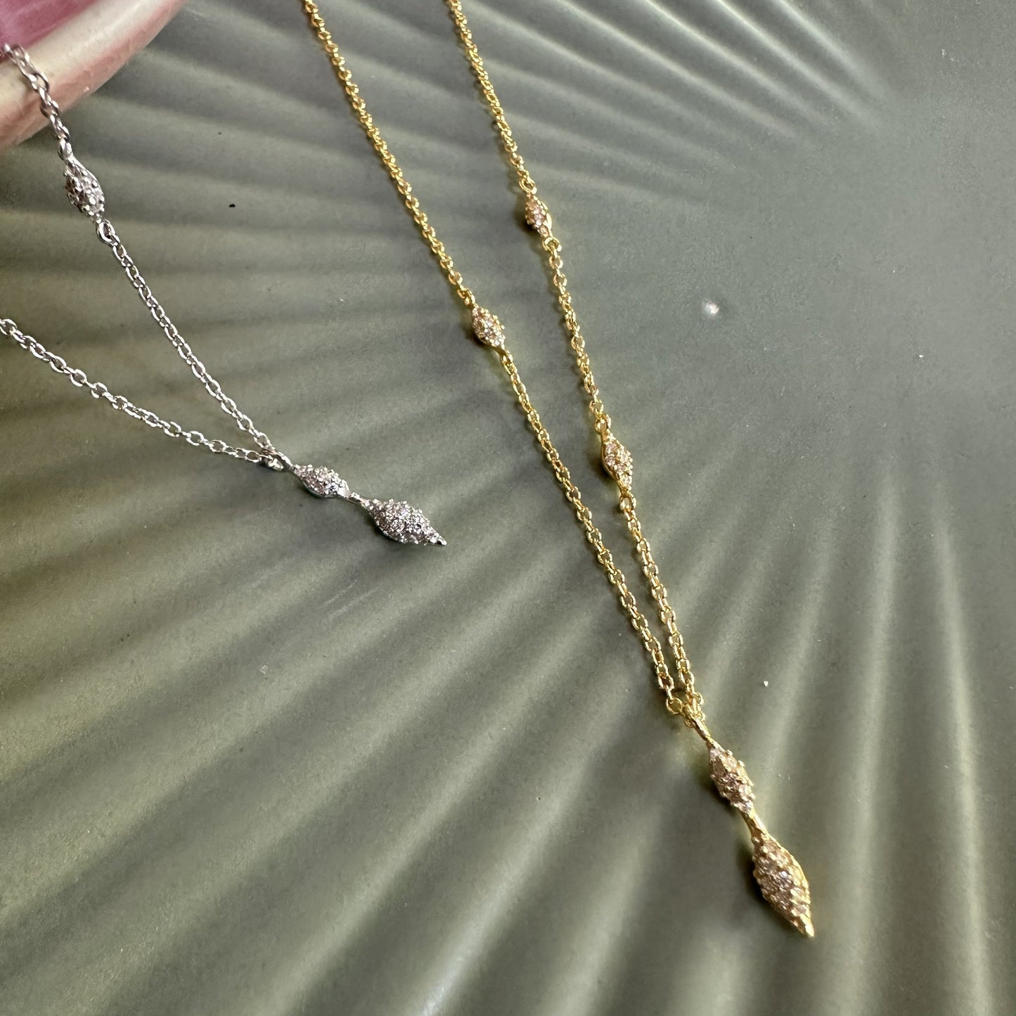 Two sparkly unusual pea pod pendant necklaces on a textured surface