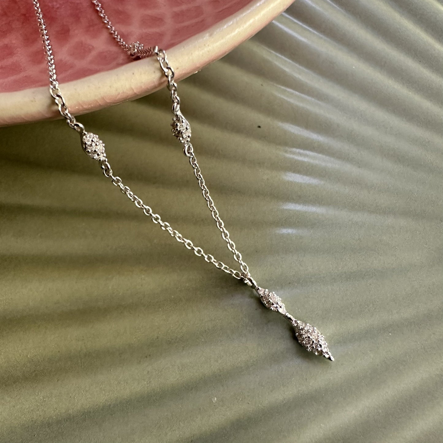 Delicate silver necklace with drop pendants on a textured surface