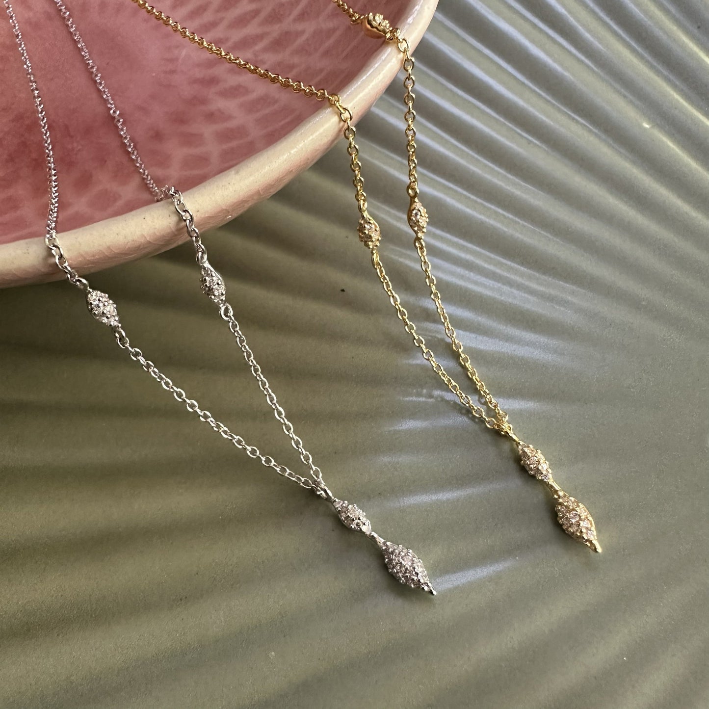 Two necklaces with modern pave set pendant drops on a textured surface
