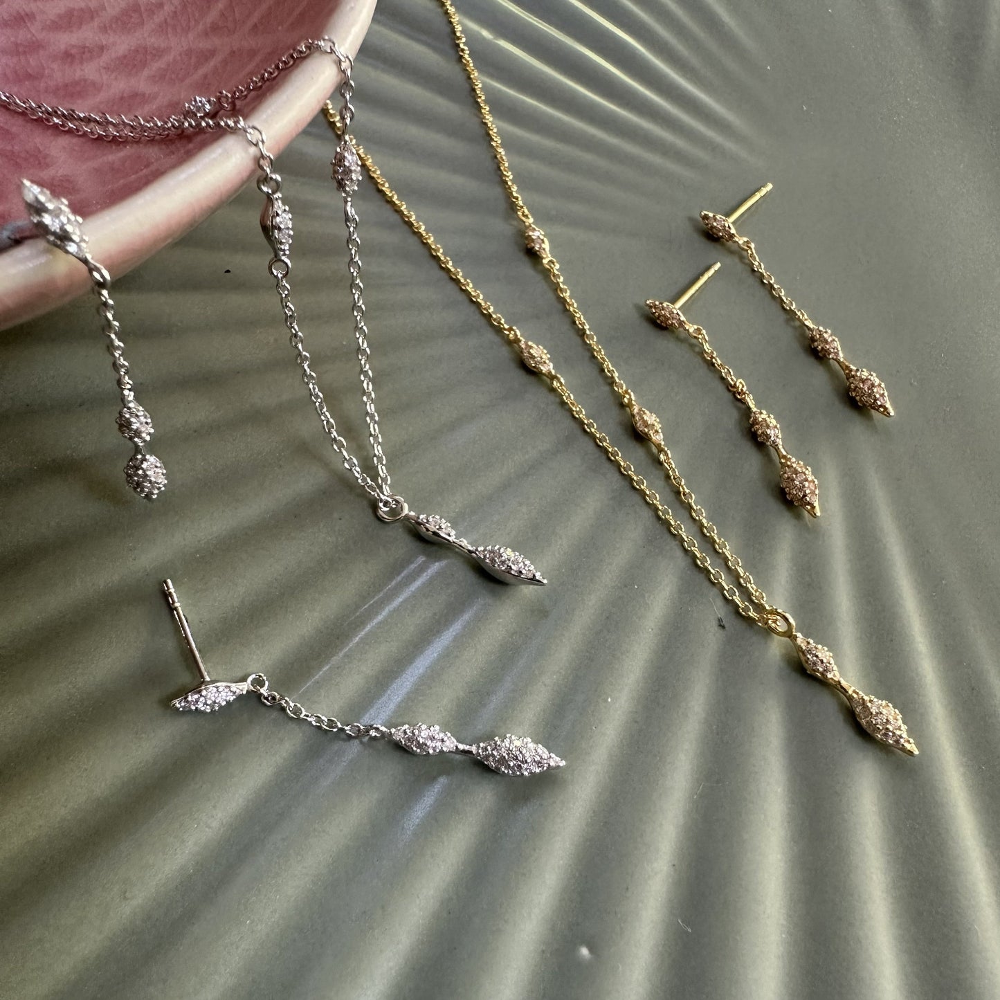 Gold and silver modern drop gemstone earrings and necklaces on a textured surface