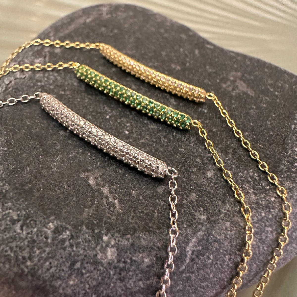 Three necklaces with different designs on a dark stone surface