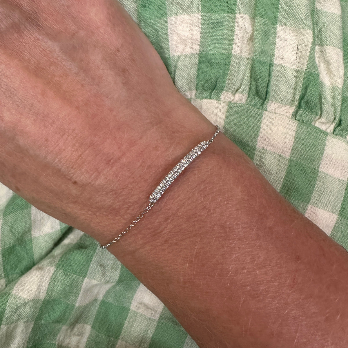 Silver bracelet on a wrist with a green checkered fabric background