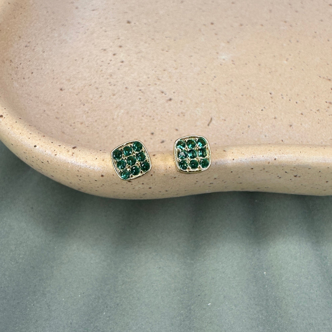 Green gemstone earrings on a beige dish with a gray background