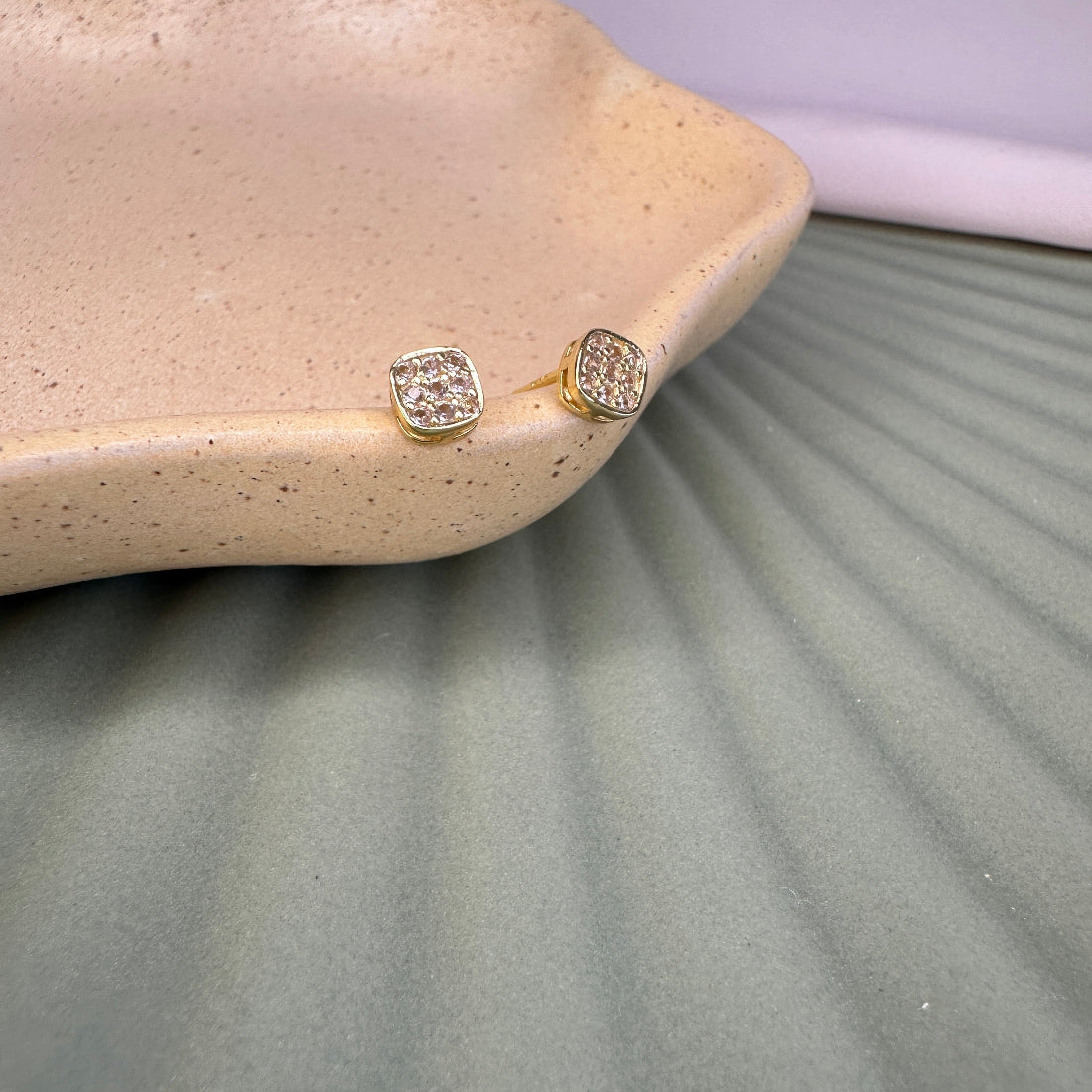 Gold earrings with  stones on a textured surfacelush colour