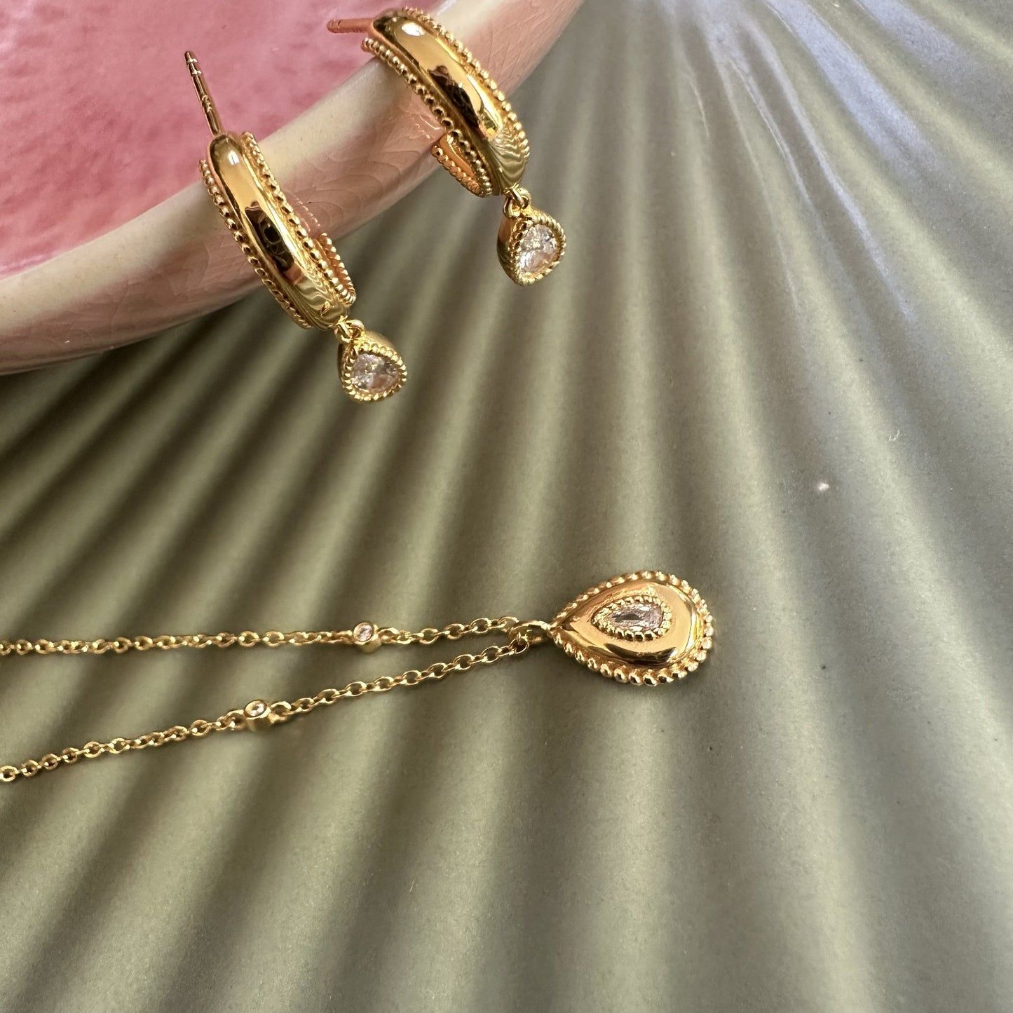 Gold hoop earrings with teardrop charm and necklace with matching teardrop on a textured surface
