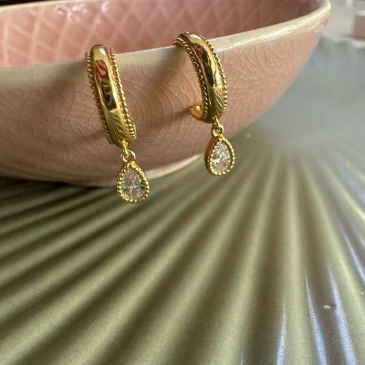 Gold hoop earrings with teardrop-shaped gemstones on a shell-shaped pink tray.