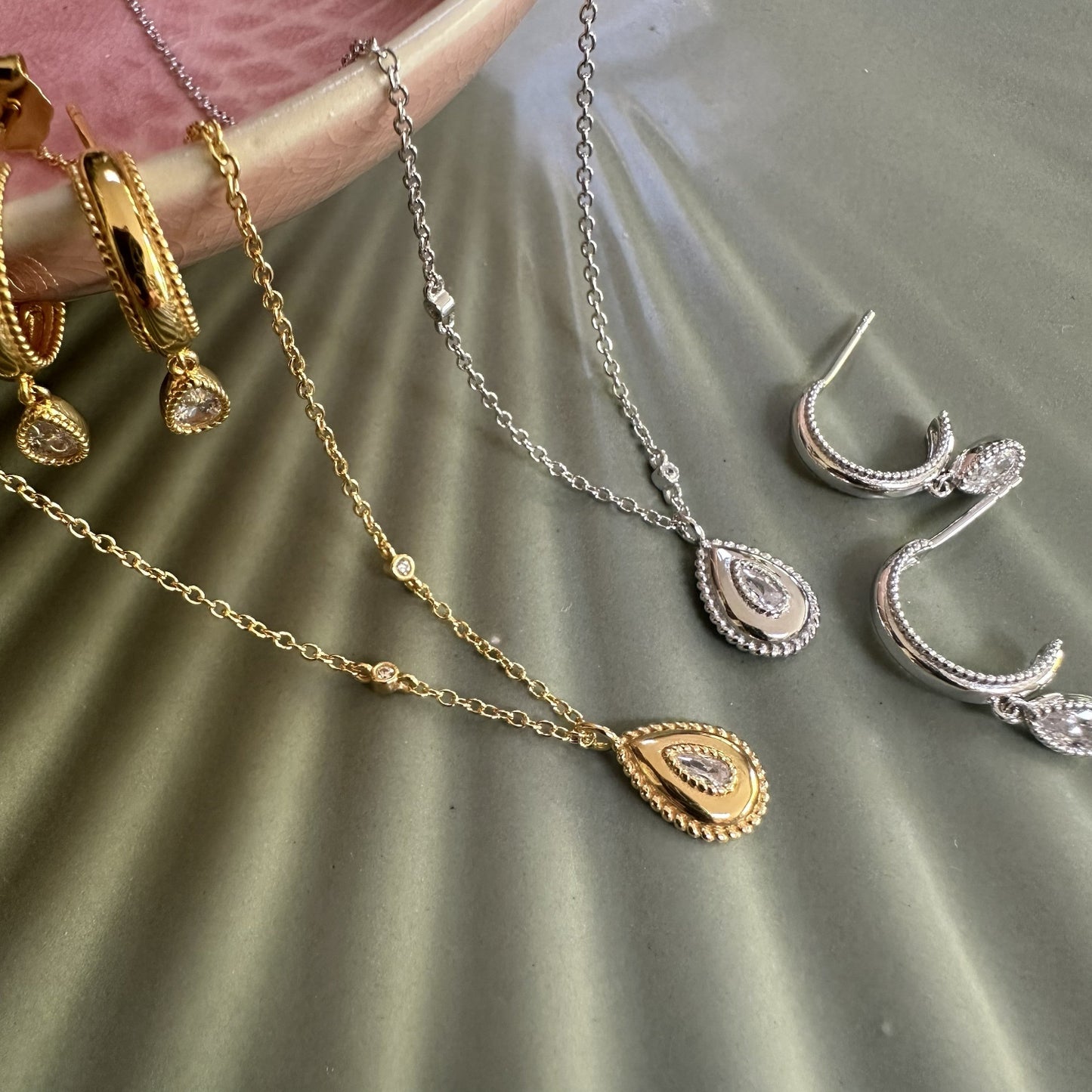 Gold and silver jewellery including teardrop pear necklaces and earrings on a green ground