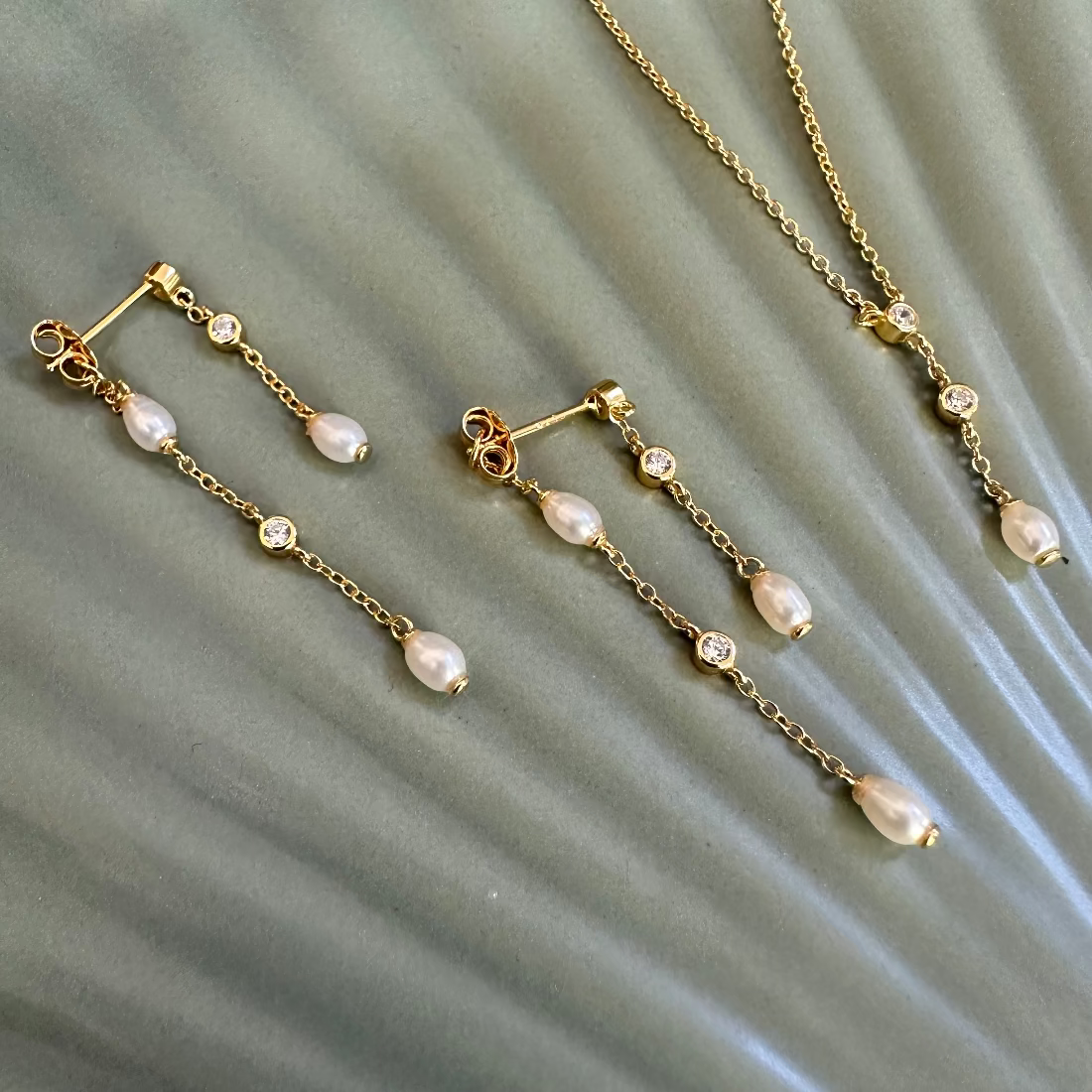 Gold necklace and earrings with natural freshwater pearls and sparkly gemstones laid on green ground