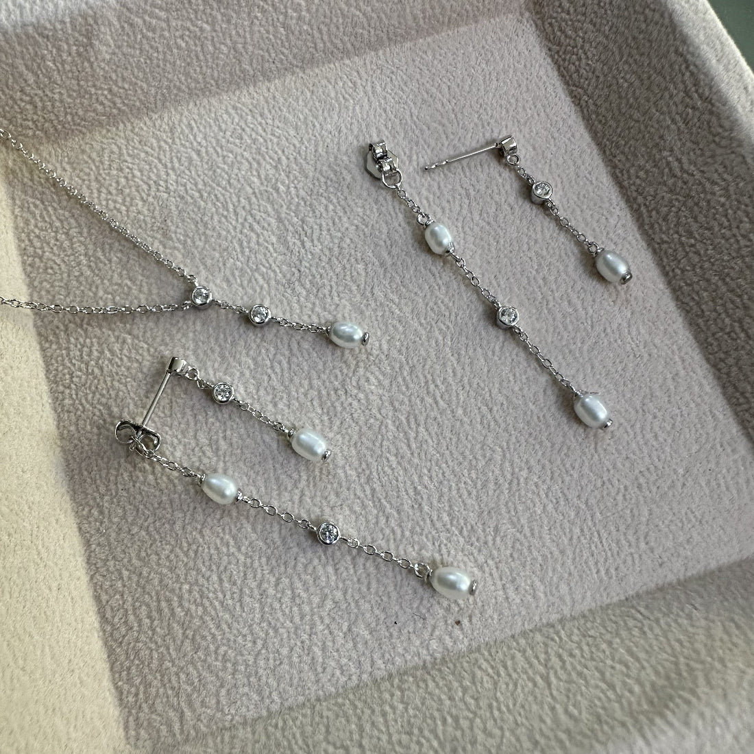 Silver necklace and matchin earrings with natural freshwater pearls and gemstones on a chain pendant on a textured surface