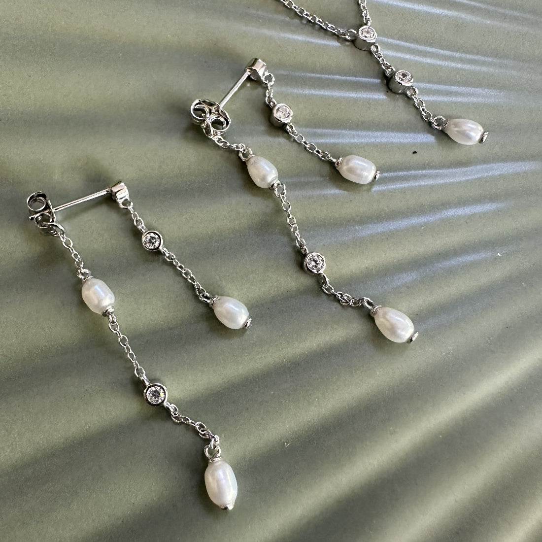 Silver earrings with pearl drops and gemstones on a textured green surface