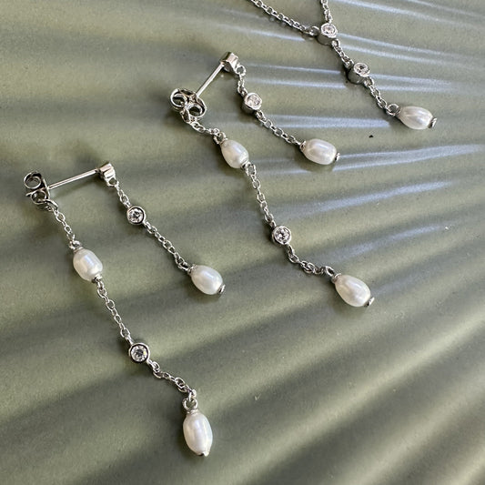 Silver earrings with pearl drops and gemstones on a textured green surface