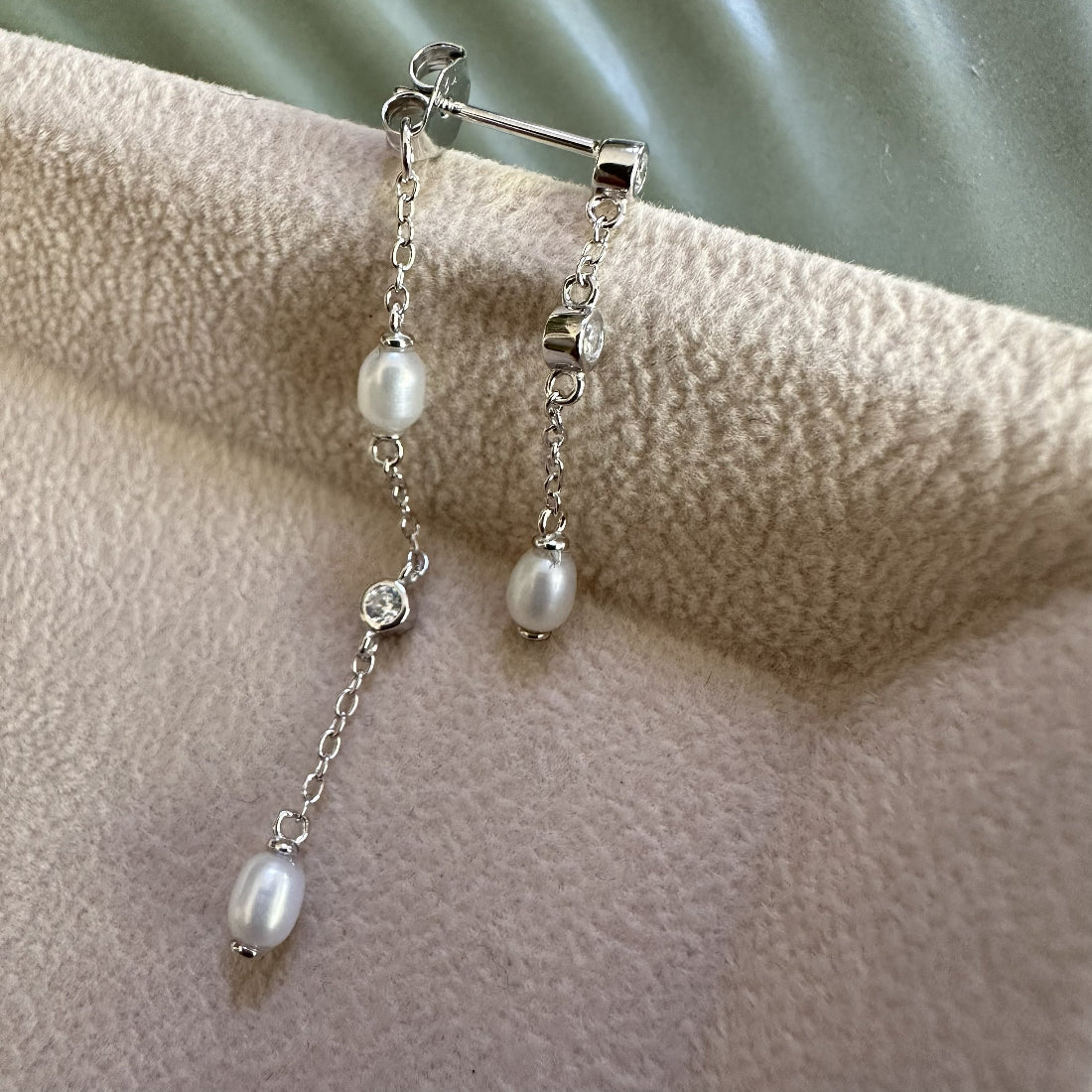 Silver earrings with real freshwater pearls and gemstones on a textured beige surface