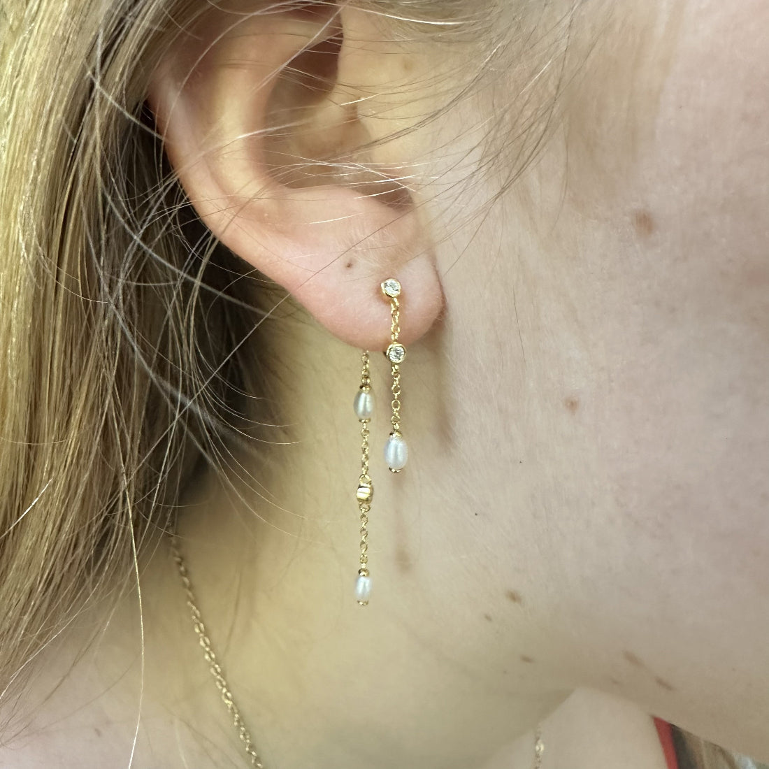 Close-up of an ear wearing a gold chain drop earring with natural freshwater pearls and sparkly cubic zirconia gemstones.