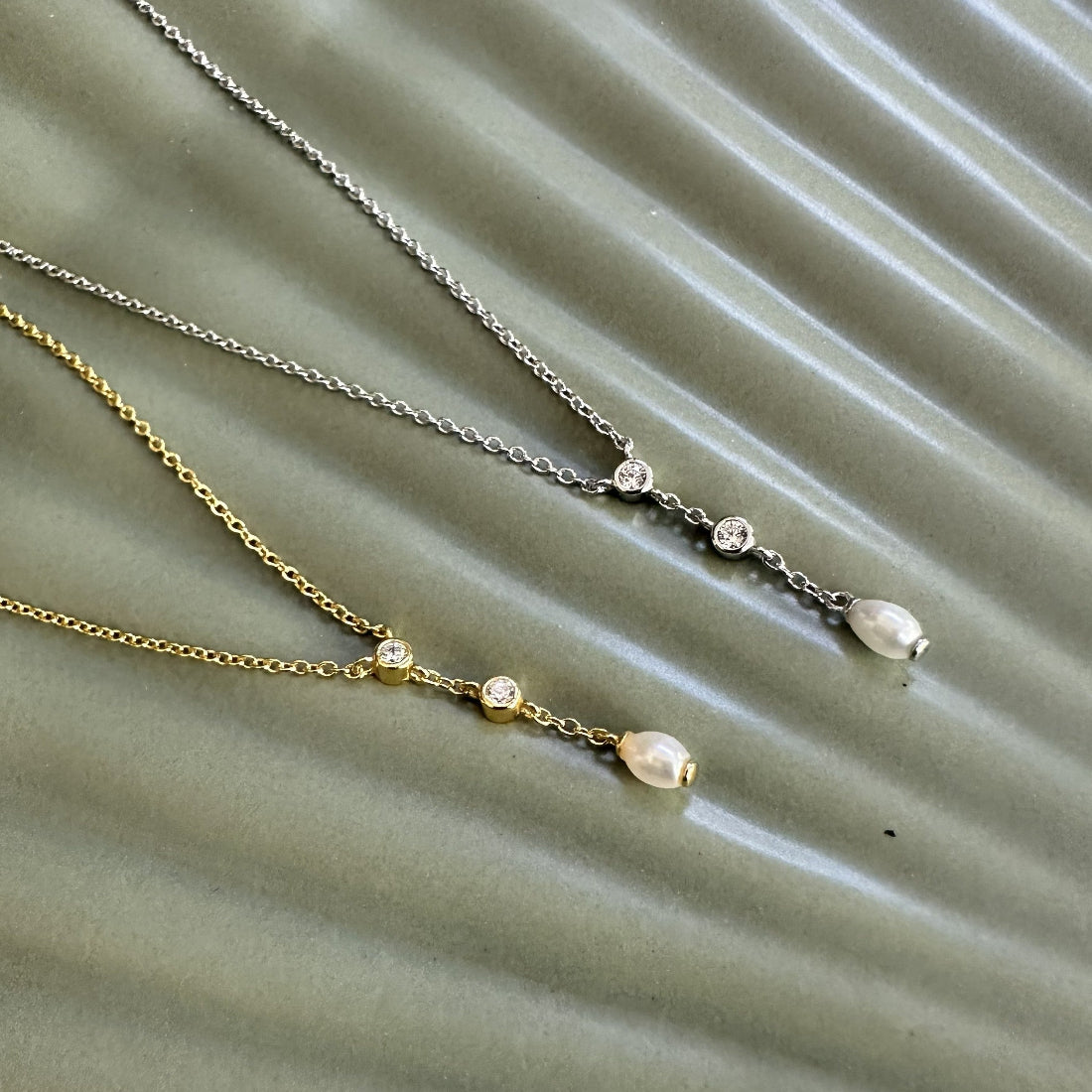Two necklaces with gemstones and a natural freshwater pearl pendant on a textured green surface