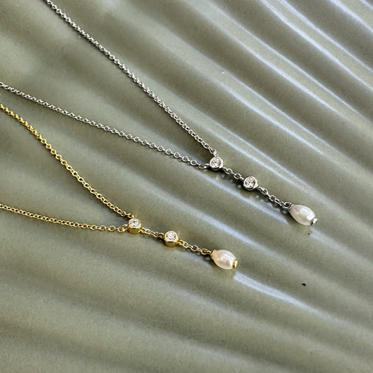 Two necklaces with gemstones and a natural freshwater pearl pendant on a textured green surface