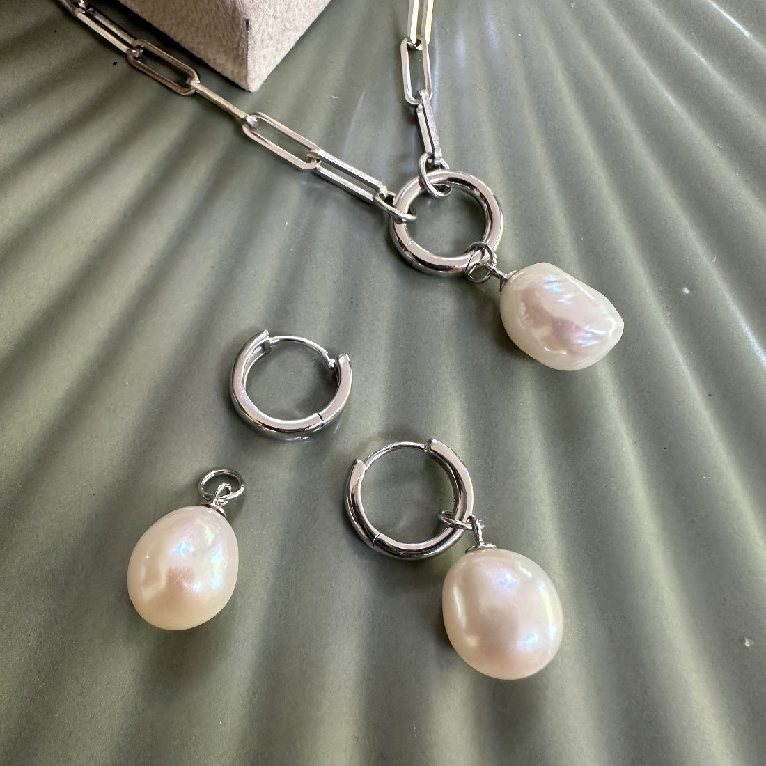 Sterling Silver huggie modern earrings with natural pearl pendants on a textured surface