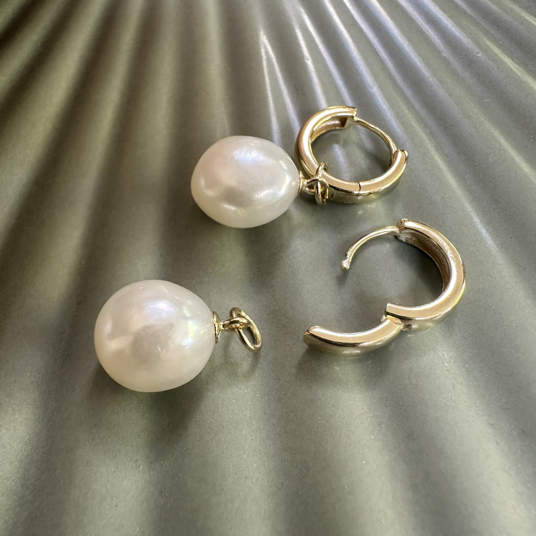 Pair of statement modern natural freshwater large pearl huggie earrings with chunky gold clasps on a textured surface