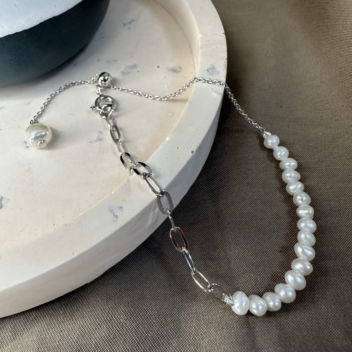 A bracelet with white freshwater pearls and an adjustable slider chain for the perfect fit, displayed on a marble surface.