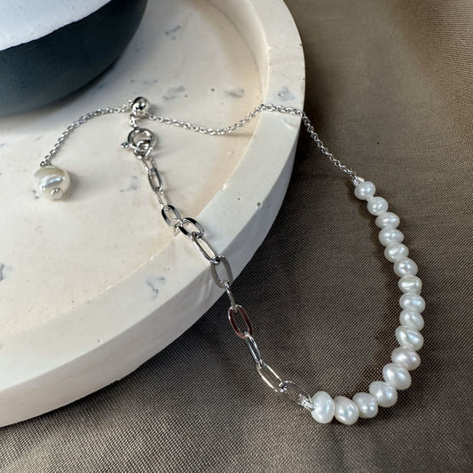 A bracelet with white freshwater pearls and an adjustable slider chain for the perfect fit, displayed on a marble surface.
