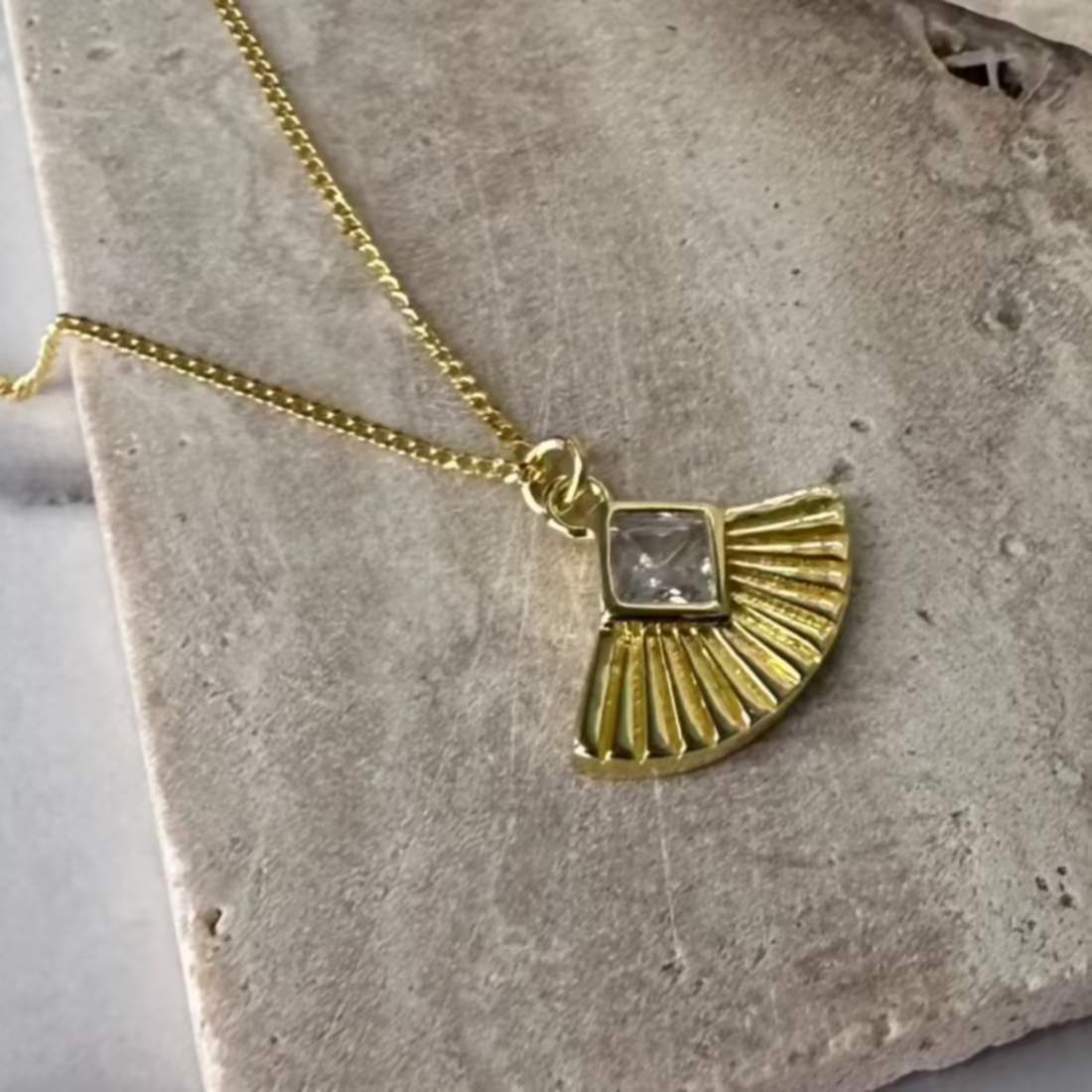 art deco inspired fan in gold with gemstone laid on marble tile