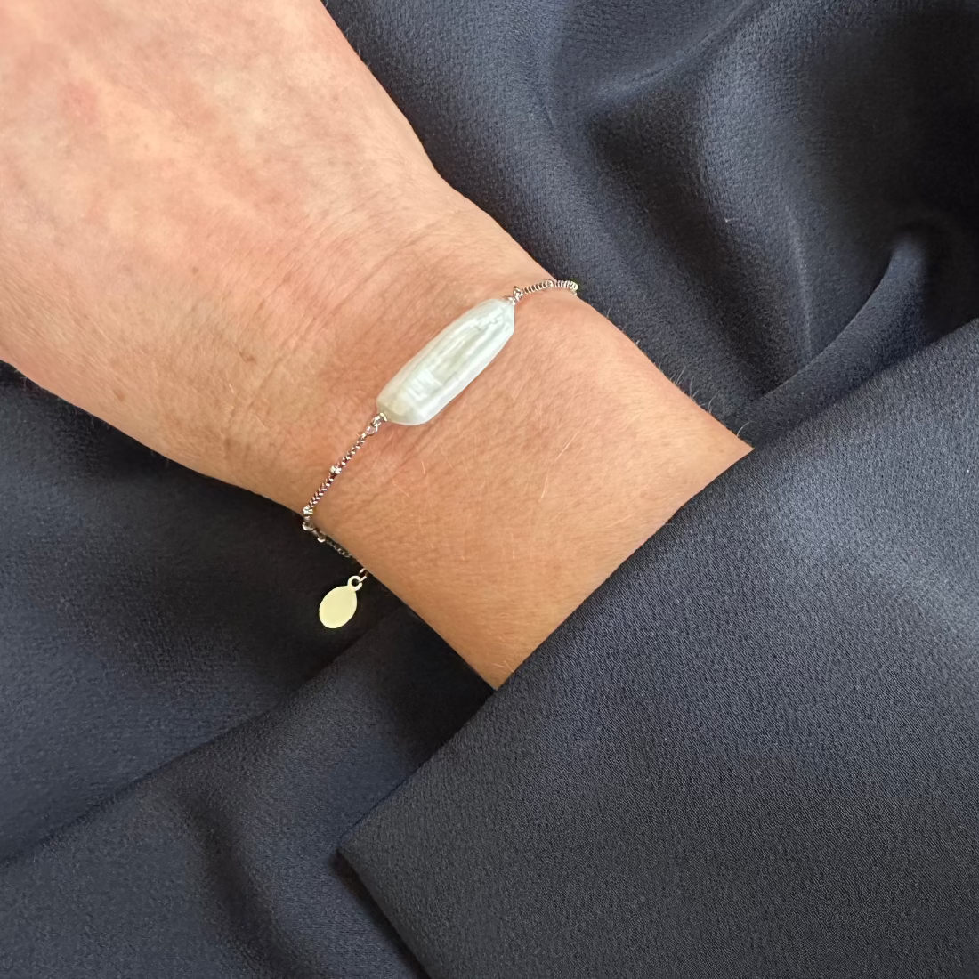 a close up wrist model wearing a freshwater pearl silver bracelet showing an organic pearl on navy dress