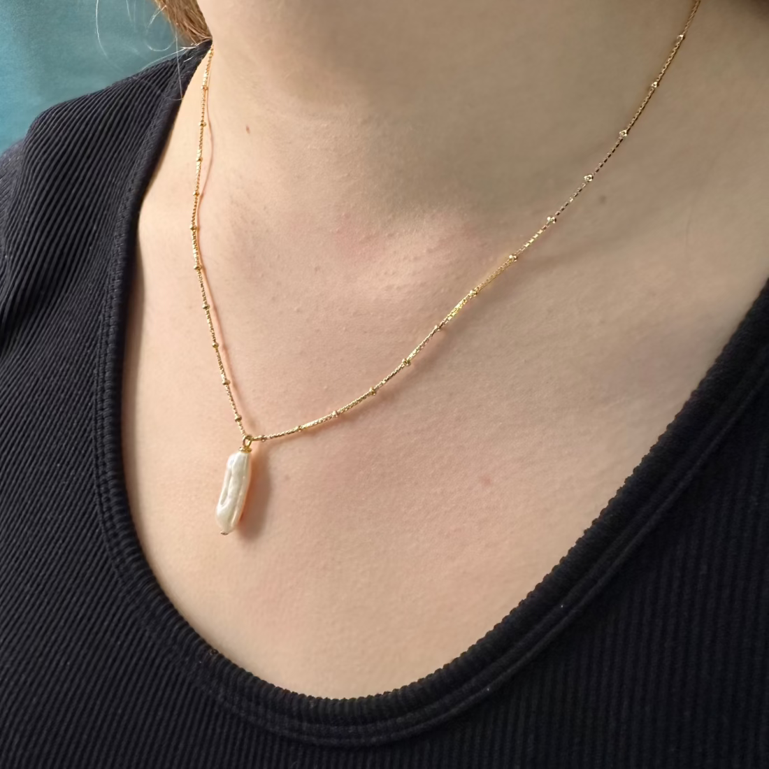 close up of mdels neck with baroque freshwatter gold pendant on ball chain necklace.