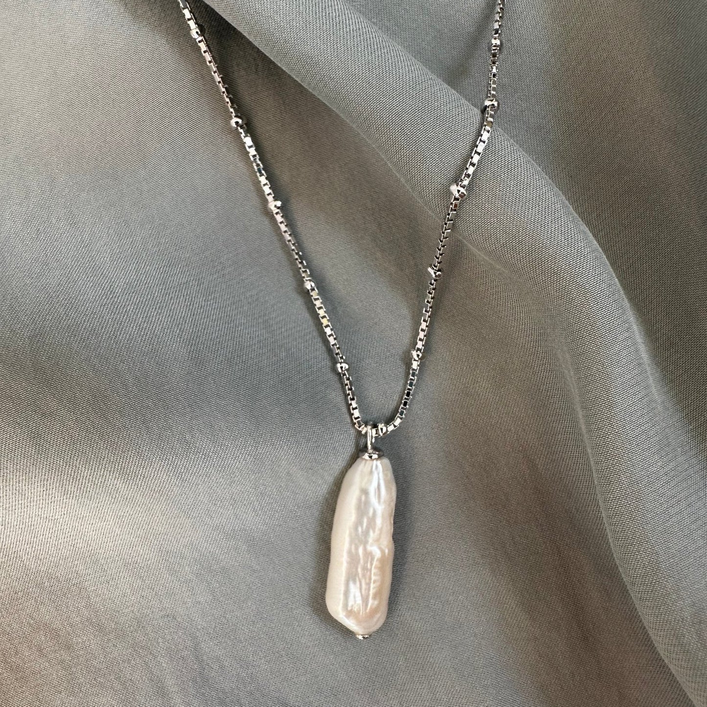 freshwater pearl pendant on satellite ball chain resting on grey fabric ground