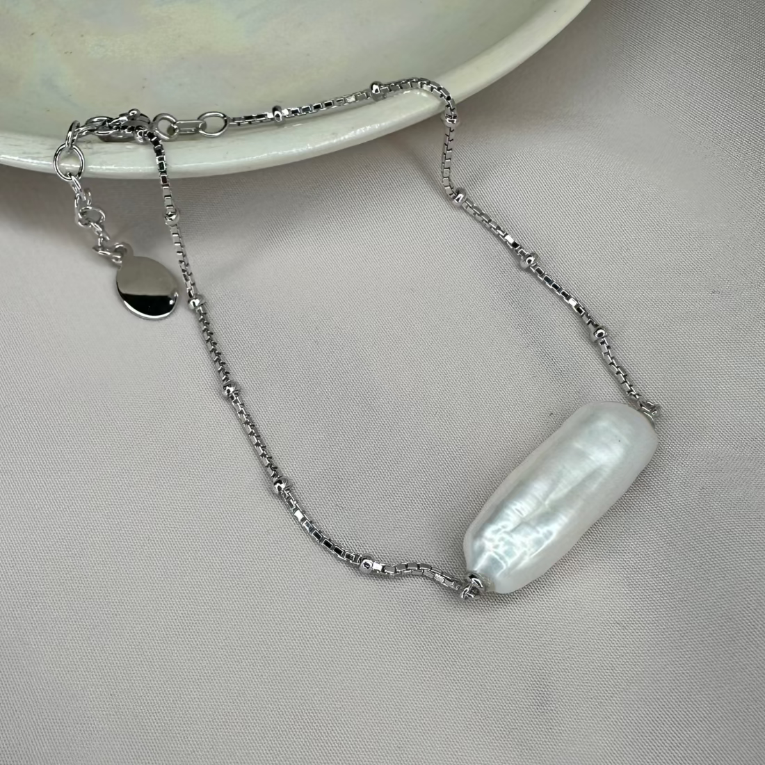 A bracelet featuring a silver satellite chain with a single freshwater baroque pearl, displayed on a pale background.