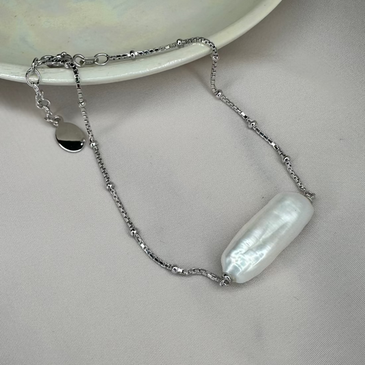 A bracelet featuring a silver satellite chain with a single freshwater baroque pearl, displayed on a pale background.