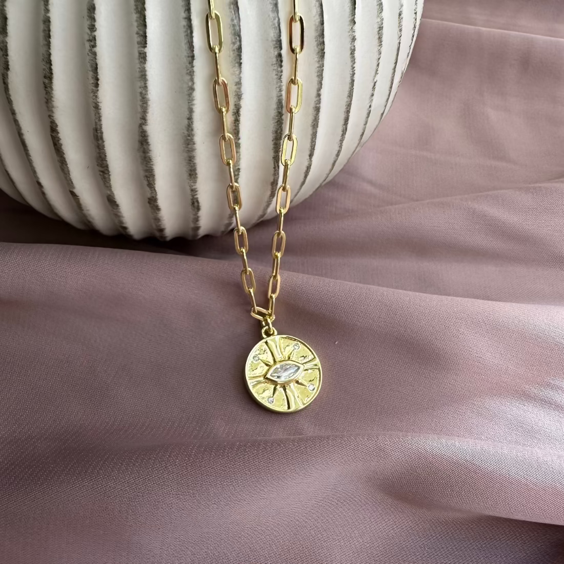 gold pendant necklace with eye gemstone on pink ground and ceramic dish