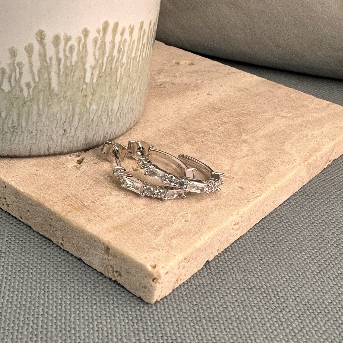 A pair of silver hoop earrings adorned with white CZ gemstones on a wooden surface.