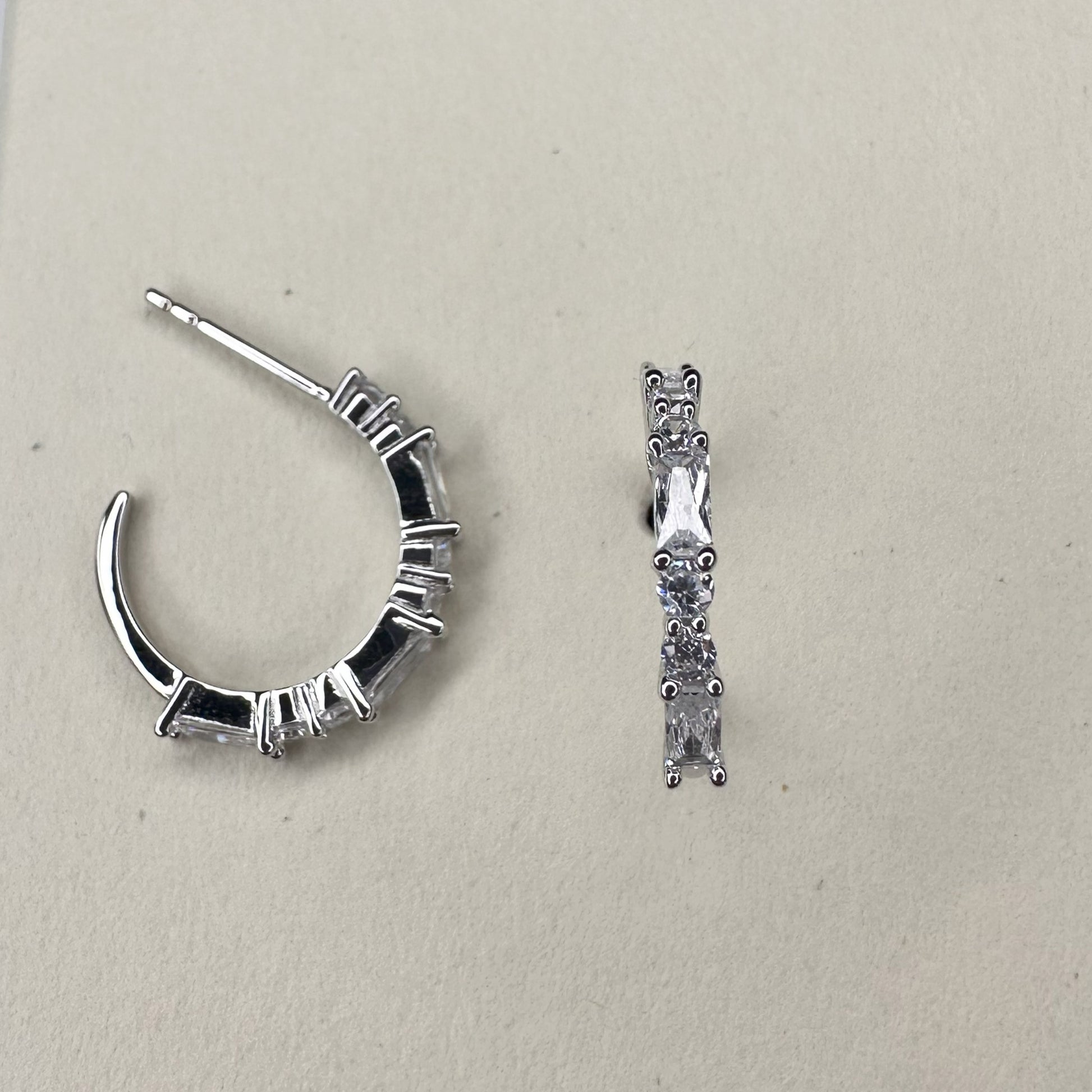 A pair of silver hoop earrings adorned with white CZ gemstones on a wooden surface.