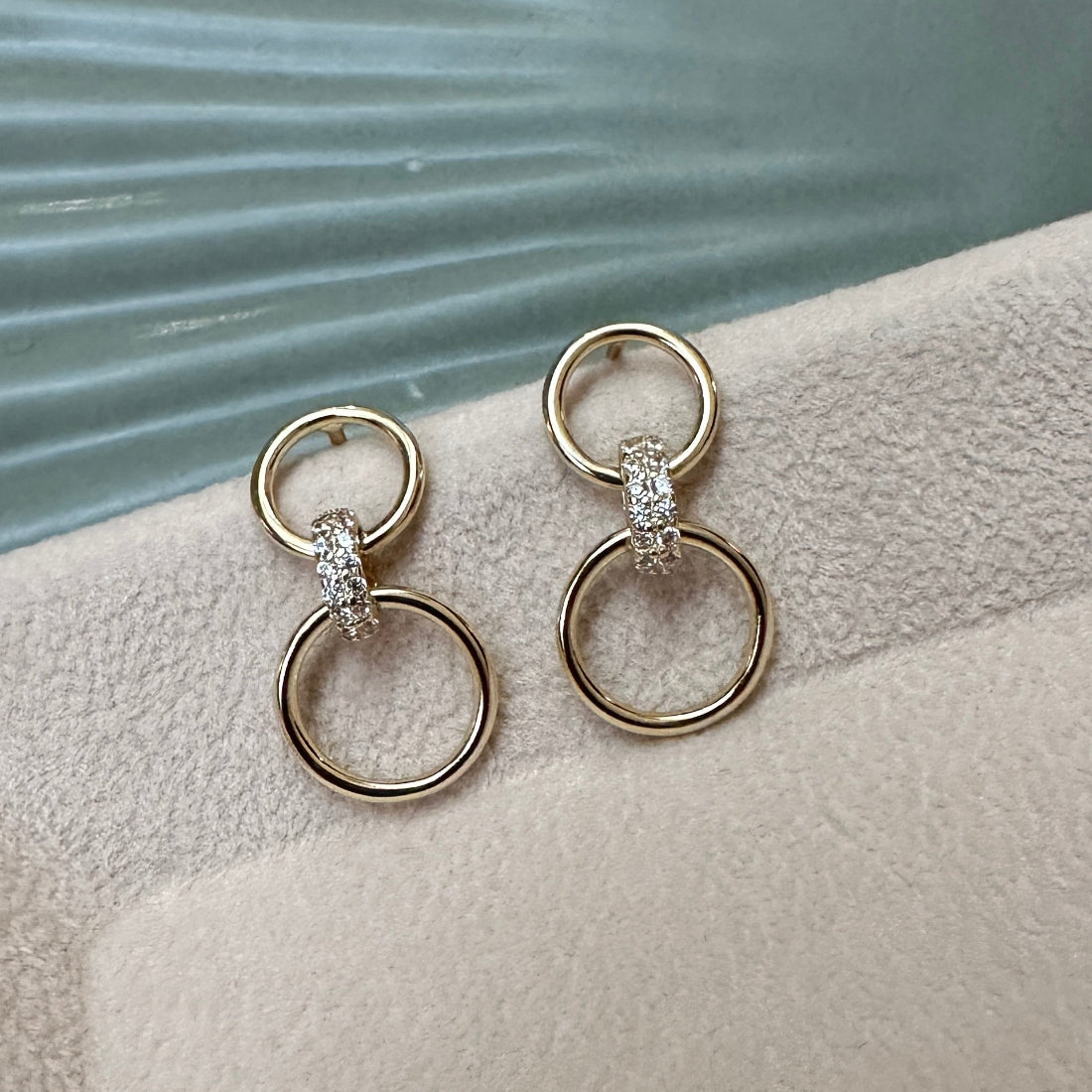 Pair of gold hoop earrings with small diamonds on a textured surface.